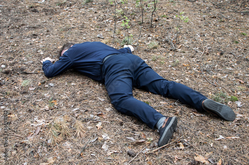 Murder in the woods. The body of a man in a blue shirt and trousers lies on the ground among the trees in the forest. Victim of an attack.