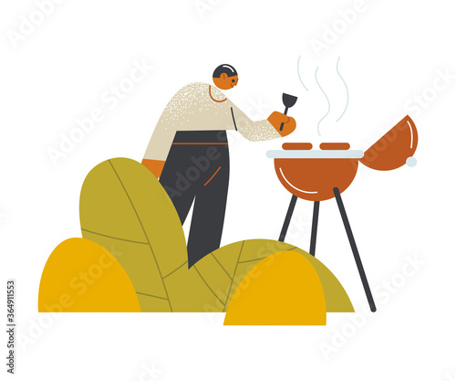 Young man making barbeque outdoors on open veranda of cafe
