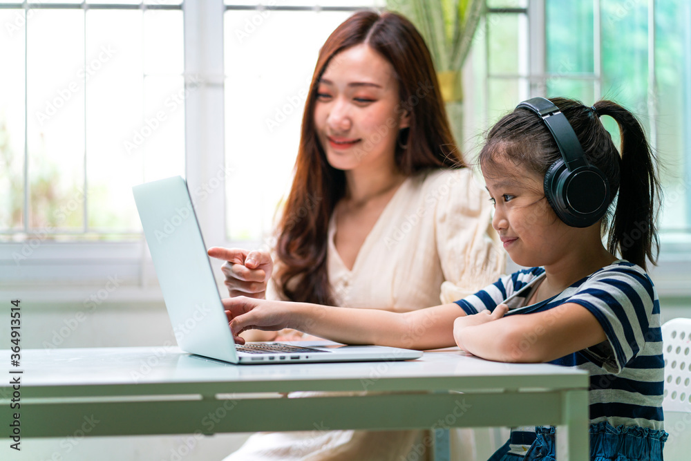 Asian girl and her mother using laptop for online study during homeschooling at home. homeschooling, online study, new normal, online learning, corona virus or education technology concept