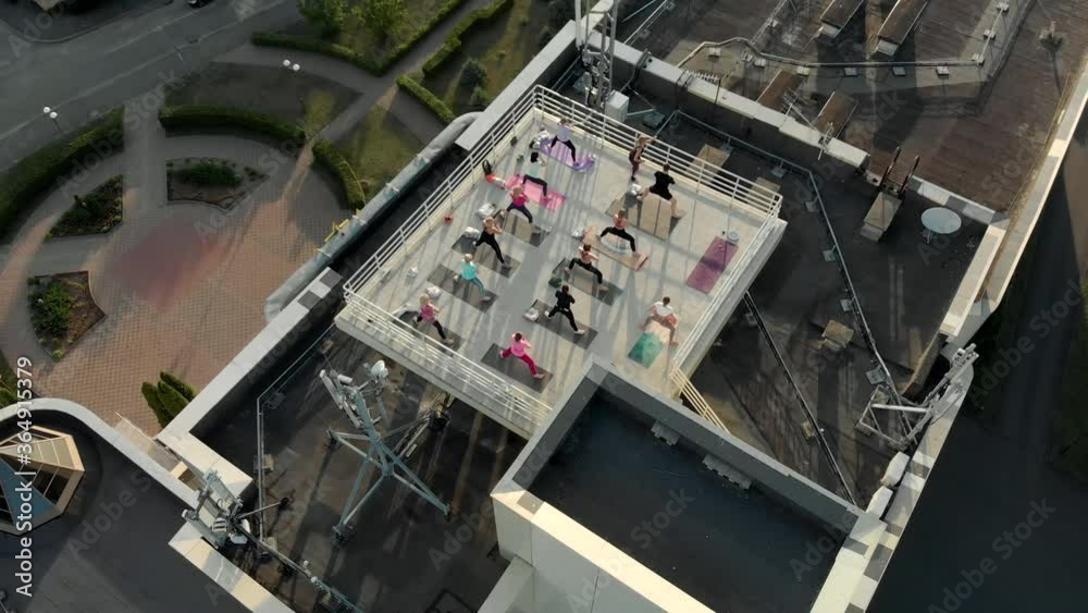 A group of fit happy people train outdoors on the roof of a high rise building, athletes do stretching on mats at sunrise in the sun A group of fit happy people train outdoors on the roof of a high rise building, athletes do stretching on mats at sunrise in the sun