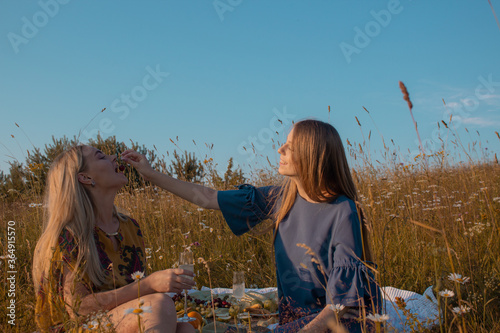 Two female friends in knitted warm sweaters having picnic in field summer. Cozy fall autumn atmosphere.