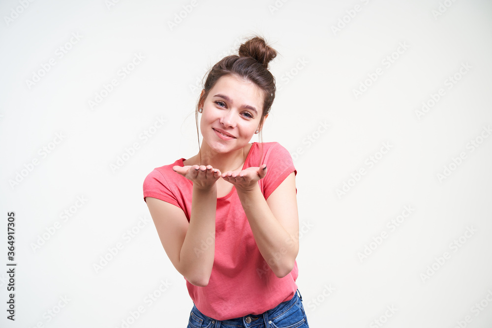 Horizontal shot of lovely young brunette female with palms up looking positively at camera with charming smile while standing against white background Horizontal shot of lovely young brunette female with palms up looking positively at camera with charming smile while standing against white background