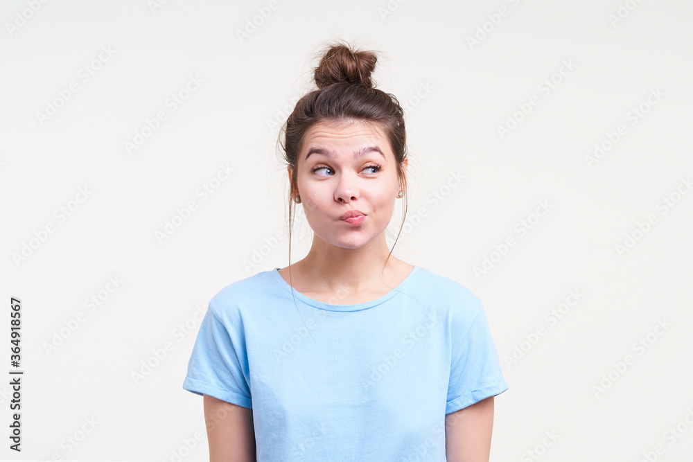 Puzzled young lovely brunette lady with natural makeup raising her eyebrows while looking wonderingly aside and pouting lips, posing over white background Puzzled young lovely brunette lady with natural makeup raising her eyebrows while looking wonderingly aside and pouting lips, posing over white background