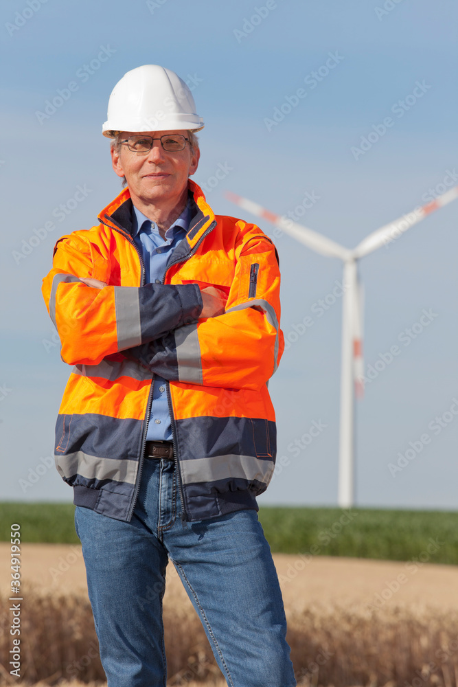 Smiling engineer with hard hat and protective clothing in front of a windmill Smiling engineer with hard hat and protective clothing in front of a windmill