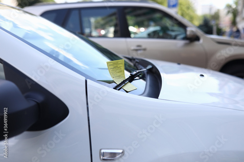 Close-up of white automobile with parking ticket under windshield wiper. Auto on street. Penalty charge notice paper. Luxury vehicle. Illegal and law concept