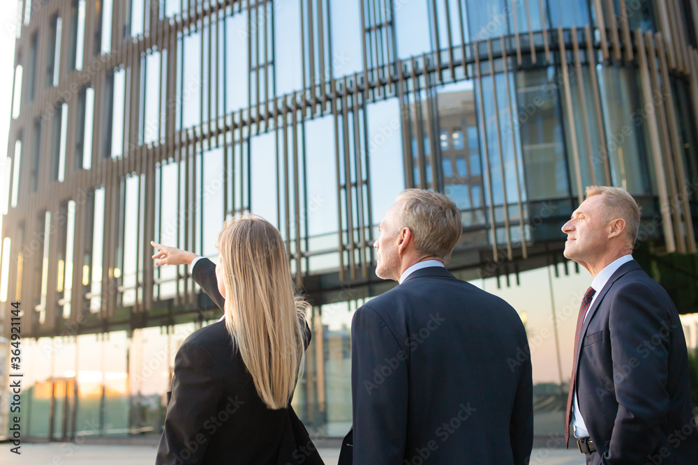 Businesspeople in suits pointing and looking at office building, discussing real property. Back view, copy space. Commercial real estate concept Businesspeople in suits pointing and looking at office building, discussing real property. Back view, copy space. Commercial real estate concept