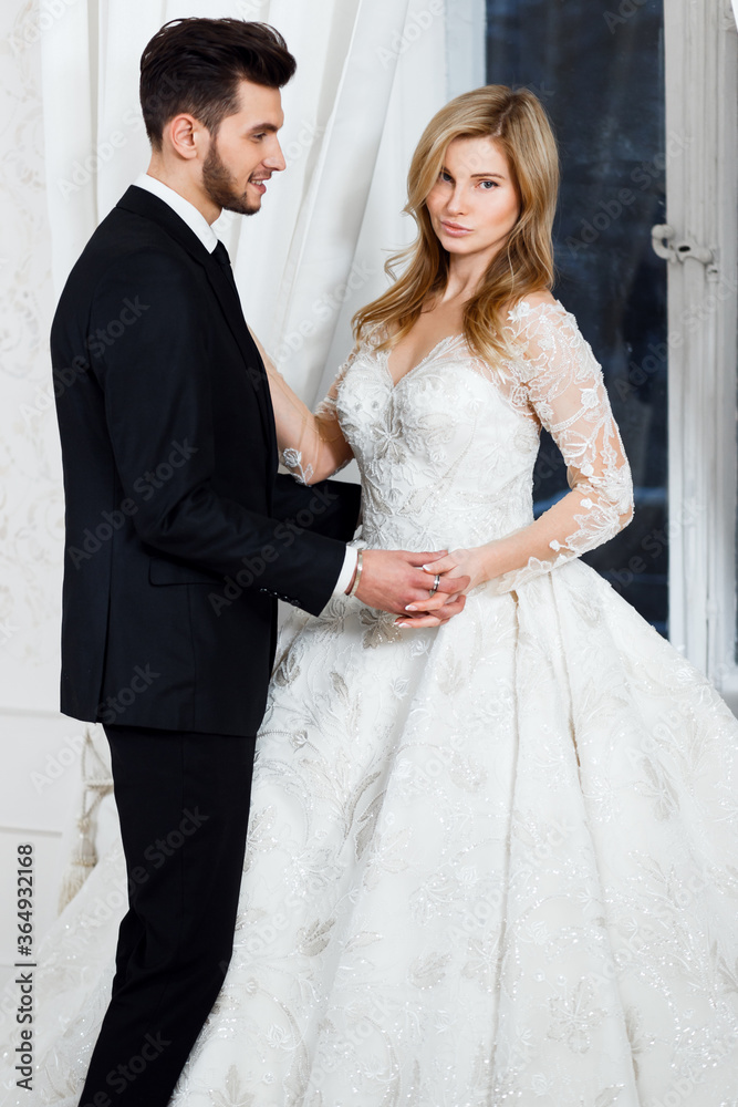 the bride and groom in a light studio are standing near the antique mirror and window. the bride and groom in a light studio are standing near the antique mirror and window.