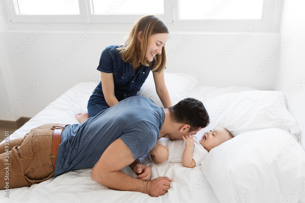 Happy young parents playing with baby on bed Happy young parents playing with baby on bed