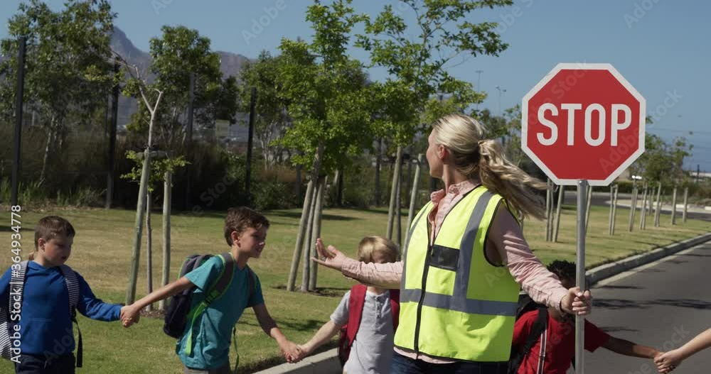 Woman with Hi-vest holding stop sign while group of kids cross the road