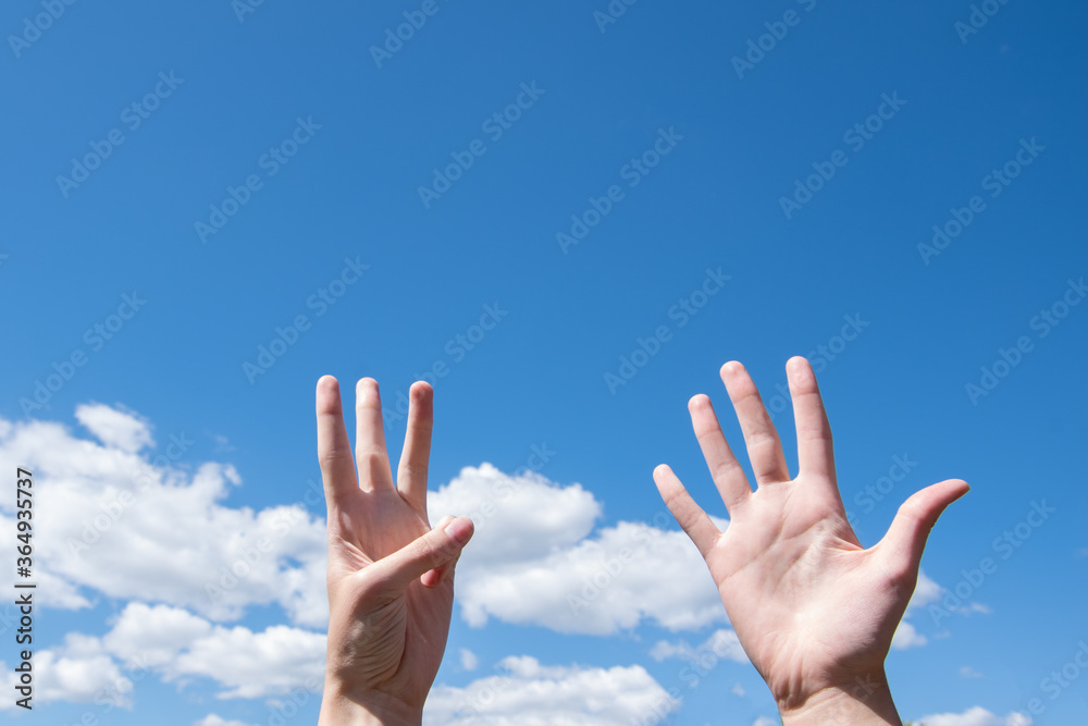 Showing a closeup of a woman's hand showing one opened palm and three fingers up isolated on a blue sky background Showing a closeup of a woman's hand showing one opened palm and three fingers up isolated on a blue sky background