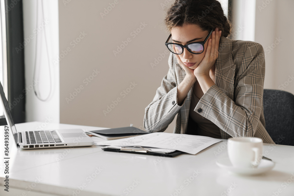 Photo of brooding brunette woman working with papers and laptop Photo of brooding brunette woman working with papers and laptop