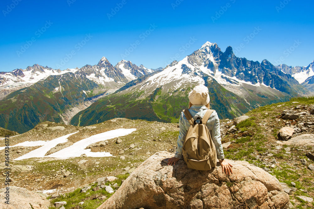 French Alps with snow in summer near Chamonix, panoramic view. Savoy tourism. Mountain trekking. Global warming, melting of snow. Female seating on stone