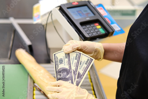 Hands in medical gloves hold euro money to buy food in the store. Bread and food are on the conveyor of the supermarket checkout