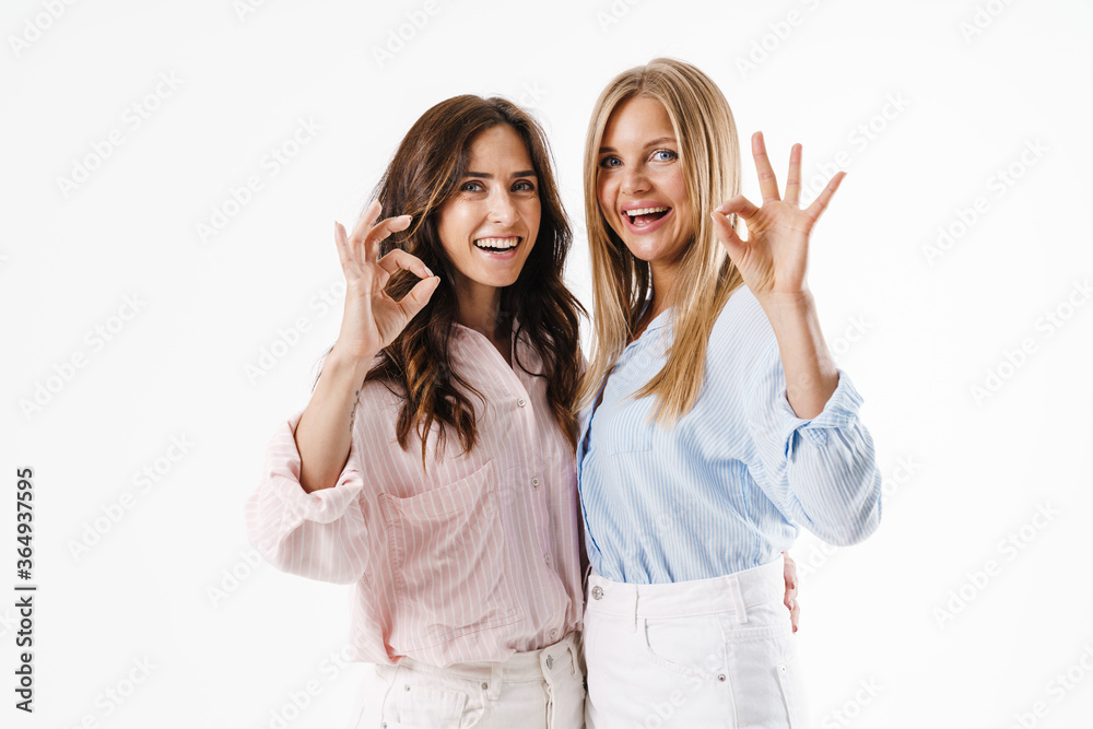 Image of smiling beautiful two women gesturing ok sign while hugging Image of smiling beautiful two women gesturing ok sign while hugging