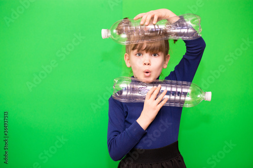 Photo of confused funny little girl holding plastic bottles and looking at camera isolated over green background