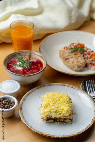 Russian cuisine: coated herring, borscht, pearl barley with fruit drink on wooden cafe table