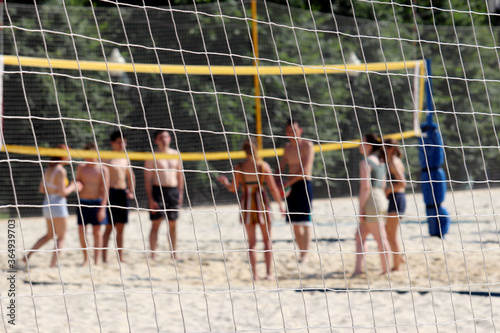 Beach volleyball, summer sport. View through a rope net to people playing ball in the sand, selective focus