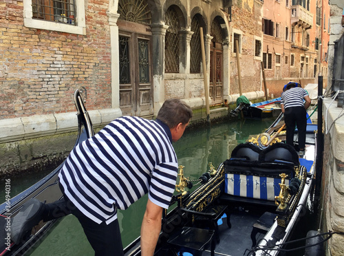 Gandoliers in striped shirts control the gandala on the water channel.. Gondoliers set sail on gondolas on a canal in Venice. photo