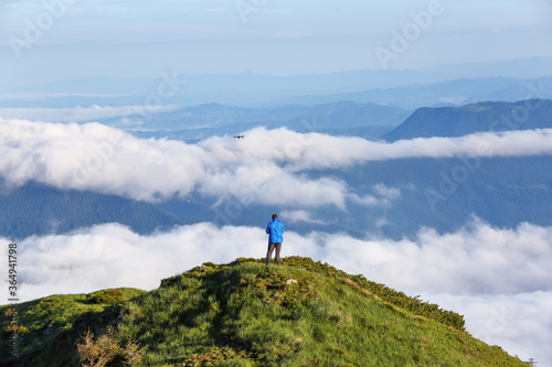 Tourist stays on the hill. Foggy summer morning. Landscape of high mountains and forests. The sun rays are shining through the fog. Wallpaper background. Free space for text.