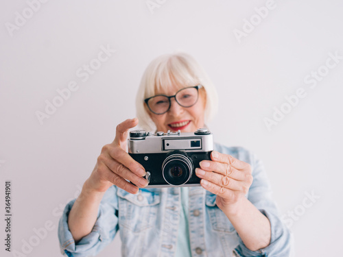 senior (old) stylish woman with gray hair and in glasses and jeans jacket taking pictures with film camera. Age, hobby, anti age, positive vibes, photography concept