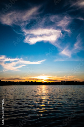 Fototapeta Naklejka Na Ścianę i Meble -  Panorama of a gorgeous sunset at a forest lake, with gold and blue color in the sky and trees reflected in the water. High quality photo