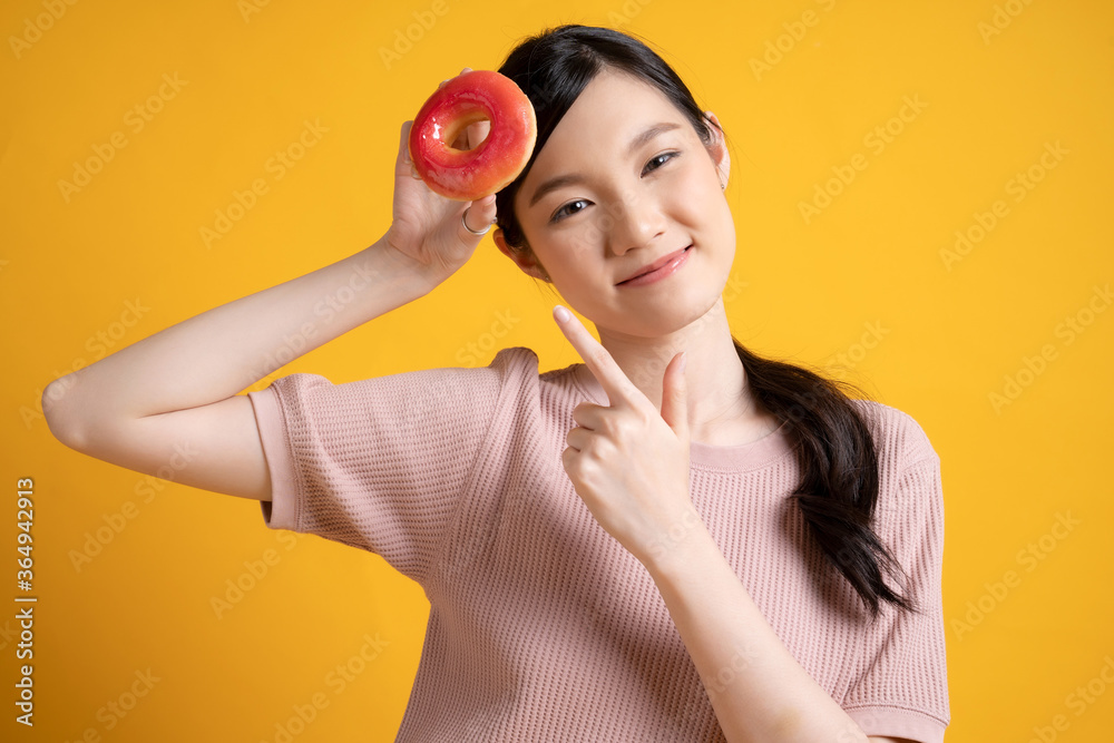 Young and cute Asian girl holding delicious donut image isolated on yellow background Young and cute Asian girl holding delicious donut image isolated on yellow background