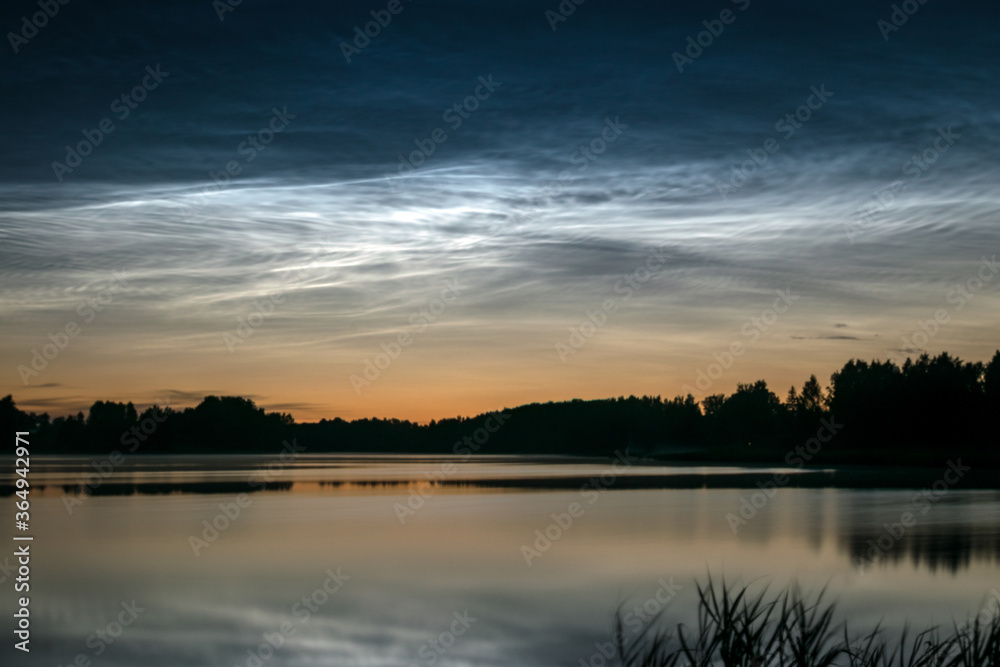 night landscape with white silver clouds over the lake, blurred foreground, charming cloud reflections in the lake water, summer night