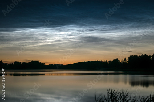 night landscape with white silver clouds over the lake  blurred foreground  charming cloud reflections in the lake water  summer night