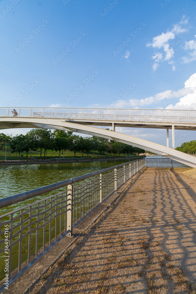 Vertical view of a bridge and fence, over canal with blue summer sky, in Juan Carlos I park in Madrid, Spain