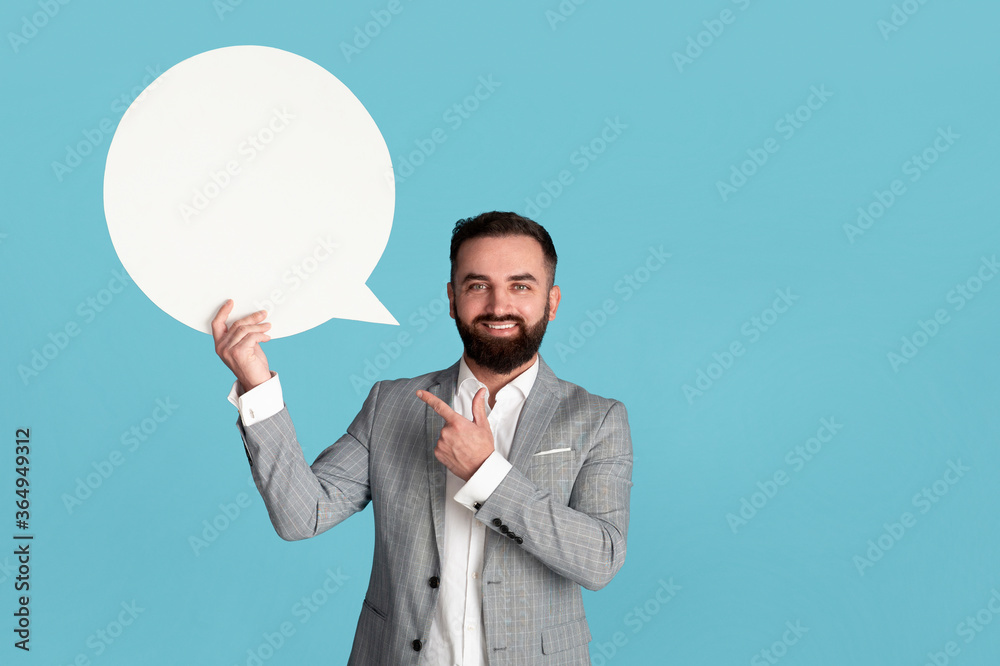 Happy young CEO pointing at blank speech bubble on blue background, space for design Happy young CEO pointing at blank speech bubble on blue background, space for design