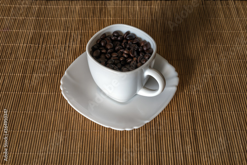 Roasted coffee grains in a white cup standing on a saucer