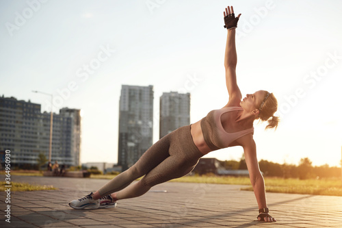 Fit strong woman standing in Side Plank pose, Vasisthasana while practicing yoga outdoors, in city. Healthy lifestyle and relaxation concept