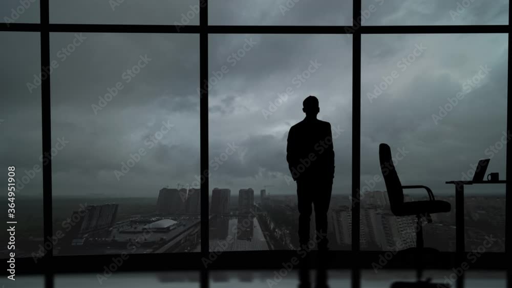 The businessman stands near the windows in his office on the grey sky background The businessman stands near the windows in his office on the grey sky background