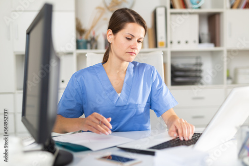 Positive female doctor working on laptop in clinic