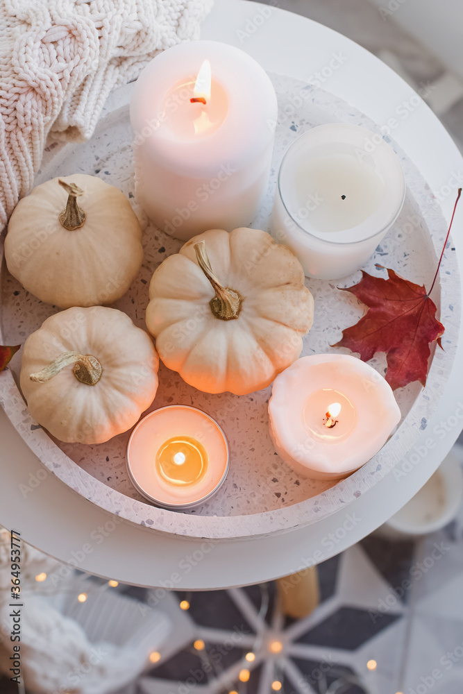 Autumn home decor with white pumpkins and burning candles.