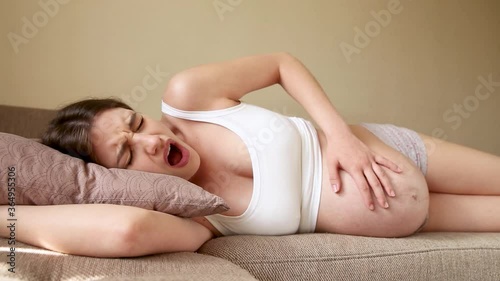 The pregnant woman is on the couch and feels pain when contractions begin