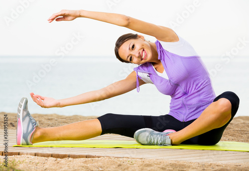 Positive young woman training yoga poses sitting on beach on sunny morning