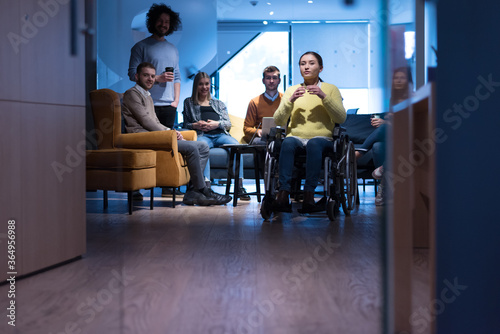 Handicapped young woman with colleagues working in office. She is smiling and passionate about the workflow. Performing in co-working space. Office people working together.