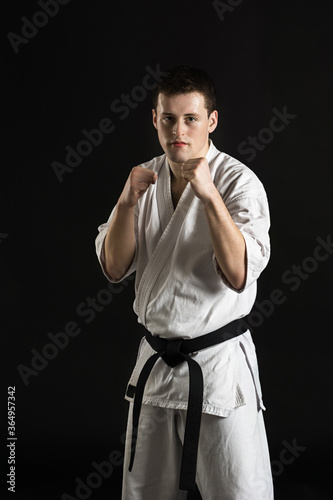 A karateka strikes or stands in a stance. Martial arts. Shidokan karate. Fighter in the studio. Kimono guy on a black background. Punch. Kick. World Karate Association the Shidokan. Black belt.