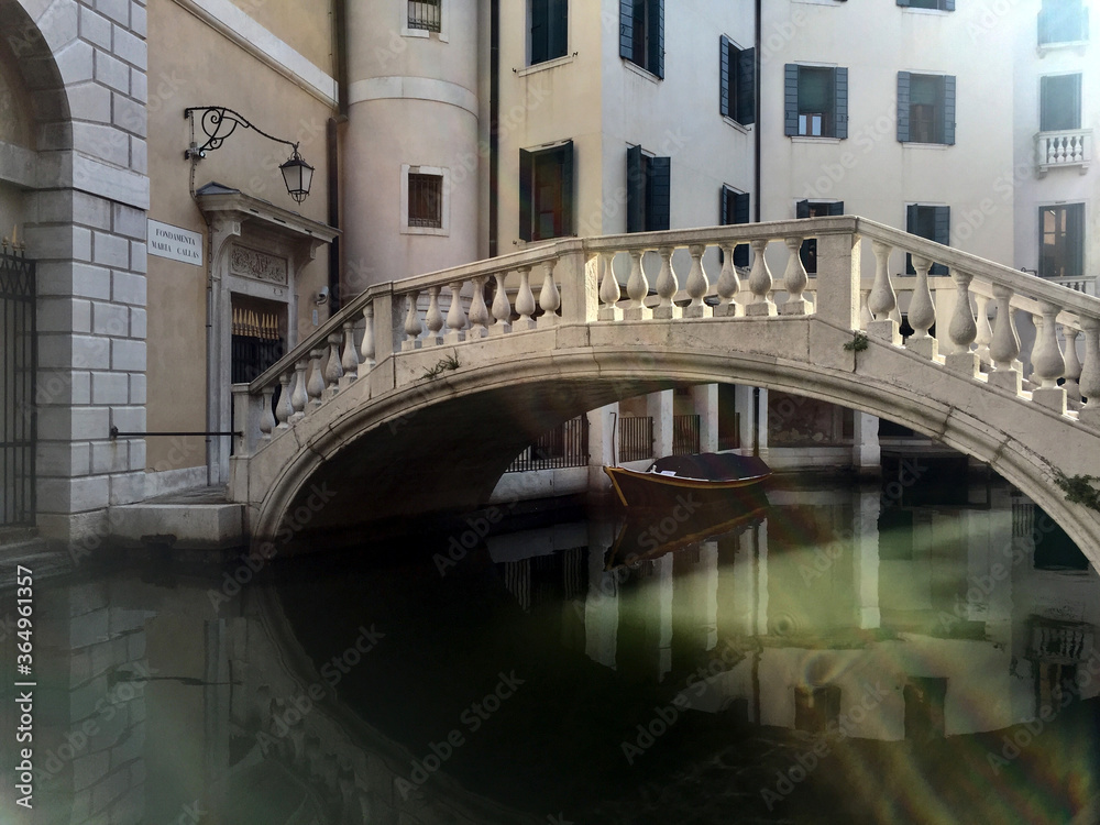Old Venetian canal bridge and boat under the bridge and water lit by sunlight.