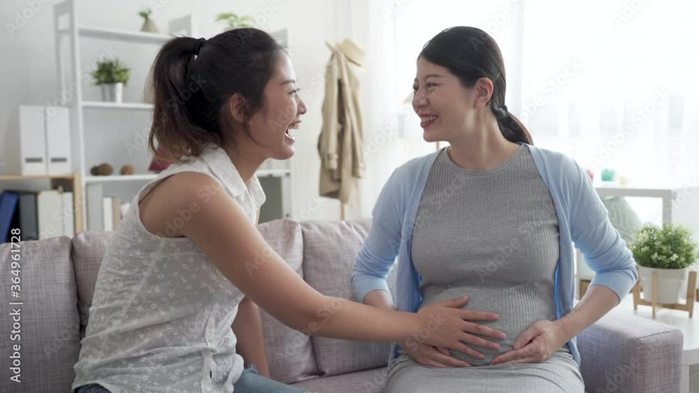 Beautiful pregnant woman and her sister spending time together in couch. charming lady listening to baby in belly of motherhood friend on sofa in home living room. cheerful two girls share happiness Beautiful pregnant woman and her sister spending time together in couch. charming lady listening to baby in belly of motherhood friend on sofa in home living room. cheerful two girls share happiness