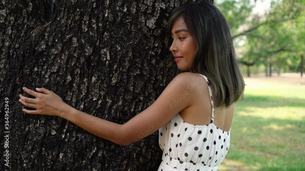 Young brunette woman hugging the big tree in the park. Beautiful girl embracing wood tree with love of nature and environment.