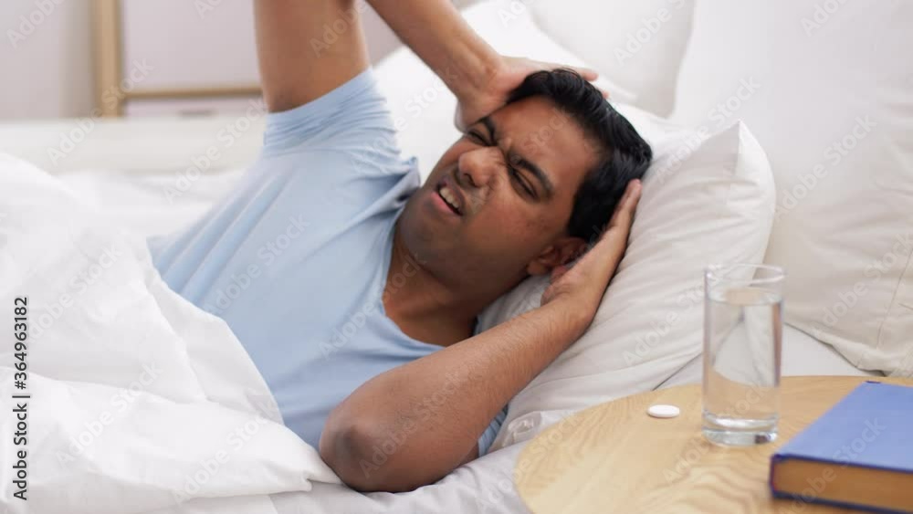 people, bedtime and rest concept - indian man lying in bed and dropping medicine pill into glass of water at home people, bedtime and rest concept - indian man lying in bed and dropping medicine pill into glass of water at home