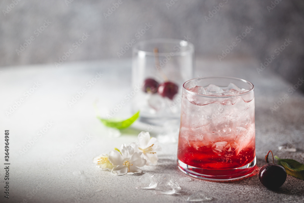 Cold cherry lemonade drink with fresh cherry and ice on gray background