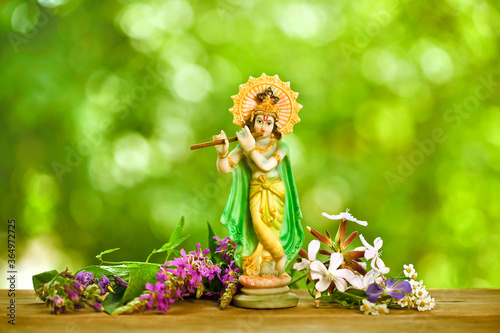 Hindu god Krishna. Statue with fresh flowers on a green bokeh background.
