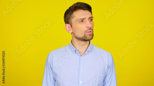 Handsome bearded man looks away on yellow background with copy space. Guy in a light blue shirt looks in place for text or goods