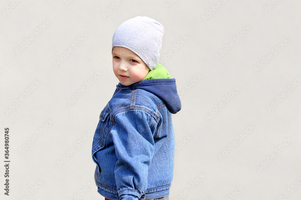 A boy in a jacket and hat posing. Fashionable child on a gray background. Child emotions A boy in a jacket and hat posing. Fashionable child on a gray background. Child emotions