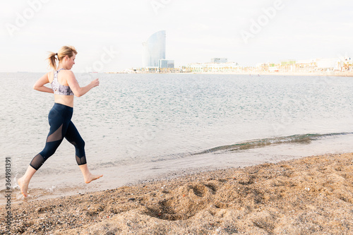 blonde sportswoman running along the beach in town