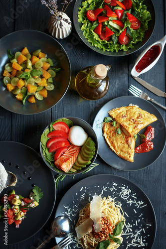 Various culinary dishes on a dark wooden table. Exquisite restaurant serve on dark dishes