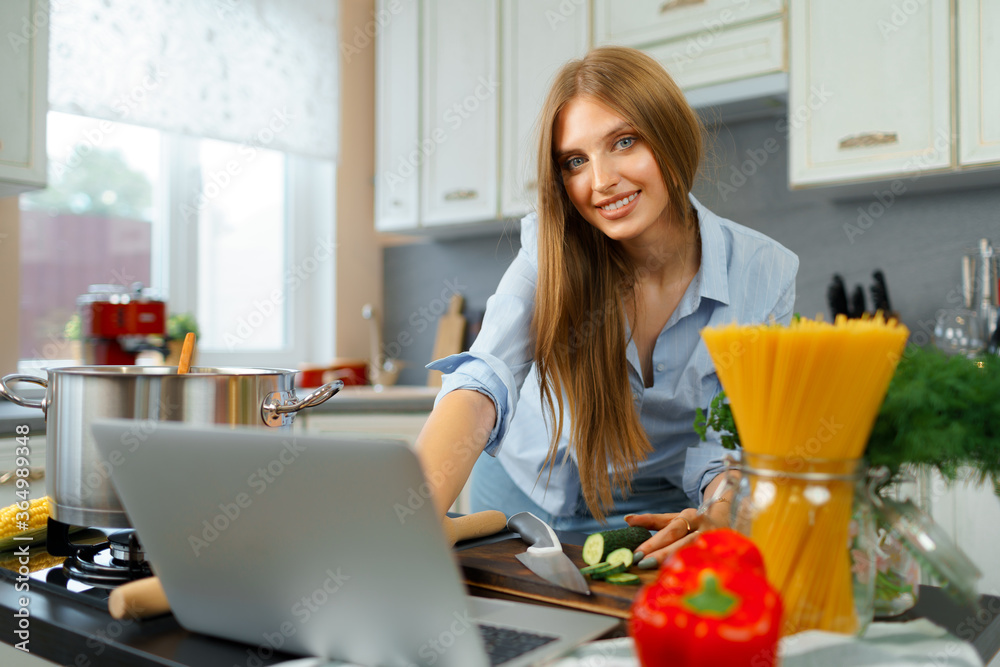 Young blonde woman with long hair using laptop in a kitchen Young blonde woman with long hair using laptop in a kitchen